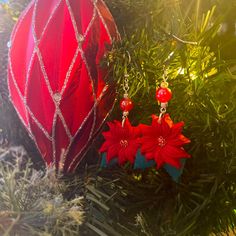 two red poinsettias are hanging from a christmas ornament on a tree