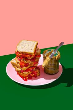 a stack of sandwiches sitting on top of a white plate next to a jar of peanut butter