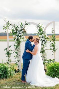 a bride and groom kissing in front of an arch with greenery at their wedding