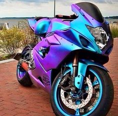 a blue and purple motorcycle parked on top of a brick road next to the ocean