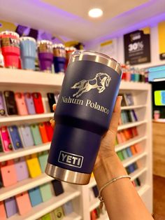 a person holding up a blue yeti coffee cup in front of a store shelf