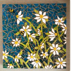 some white flowers and a yellow bee on a blue mosaic tile wall art piece with gold accents