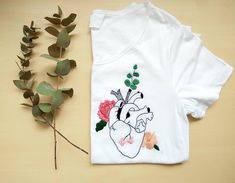 a t - shirt with an image of a heart and flowers on it next to a plant