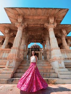 a woman in a pink and white dress is standing outside an old building with pillars