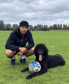 a man kneeling down next to a black dog with a soccer ball in it's mouth