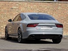 the rear end of a silver car parked in front of a brick wall on a street