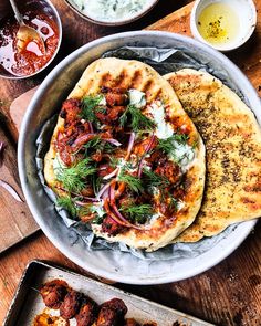 two pita breads with various toppings and sauces on the side sitting on a wooden table