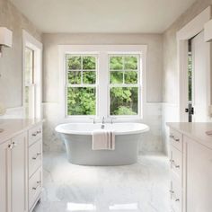 a white bathroom with a large tub and two windows that look out onto the trees