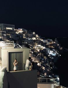 two people standing on the roof of a building at night with city lights in the background