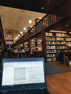 an open laptop computer sitting on top of a wooden table in front of a library filled with books