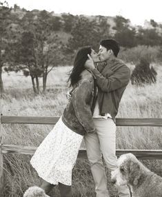 a man and woman kissing in front of a fence with two poodles on the ground