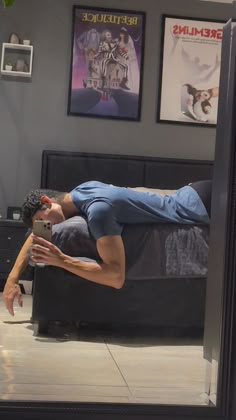 a man laying on top of a bed next to a black dresser under a mirror