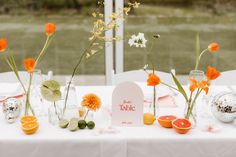 the table is set up with oranges, flowers and vases on it for a wedding reception