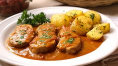 a white plate topped with meat covered in gravy next to potatoes and parsley