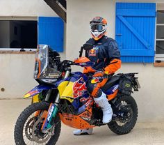 a man in an orange and black jacket is sitting on a dirt bike with blue shutters