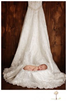 a baby is laying on the floor in front of a wedding dress hanging from a wooden wall