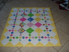 a yellow and white quilt is on the floor next to a tiled floor with tiles