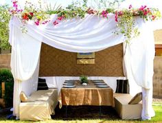 an outdoor dining area is decorated with white drapes and flowers