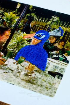 a blue bird sitting on top of a wooden table next to a white framed photo