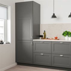 a kitchen with gray cabinets and white counter tops, along with potted plants on the window sill