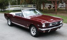 a maroon mustang convertible parked in a parking lot next to a tree and grass area