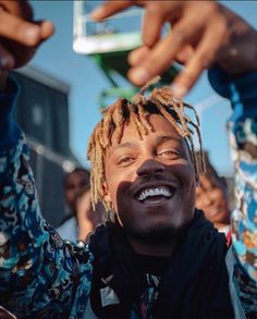 a man with dreadlocks smiles and holds his hands up in the air