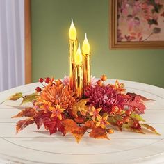 two candles are lit on a table with autumn leaves