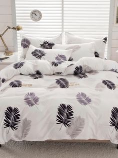 a bed with white sheets and purple palm leaves on the comforter in front of a window