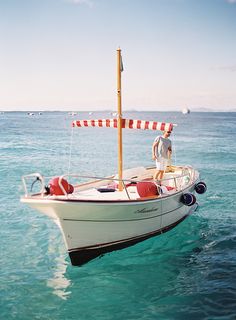 a man standing on the bow of a small boat in clear blue water with red and white stripes