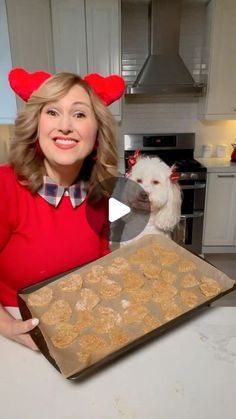 a woman holding a pan with cookies in it and a dog standing next to her