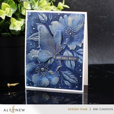 a close up of a card on a table with flowers and plants in the background