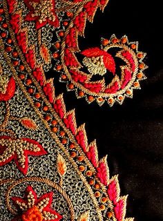 closeup of an embroidered fabric with red and gold designs on black background, showing the detailed details