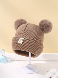 a brown hat with two pom - poms sitting on top of a white stand