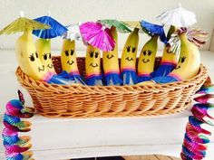 bananas with faces drawn on them sitting in a basket filled with umbrellas and decorations