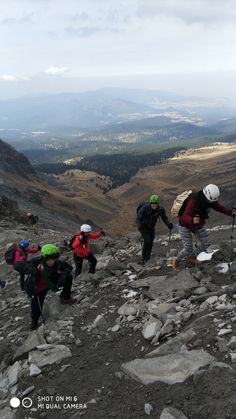 several people hiking up a rocky hill with mountains in the background