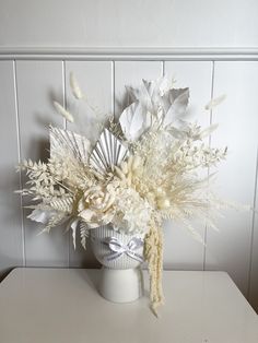 a white vase filled with lots of flowers sitting on top of a table next to a wall