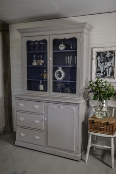 a gray china cabinet with glass doors and drawers in a room that has pictures on the wall