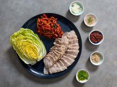 a black plate topped with meat and veggies next to bowls of sauces