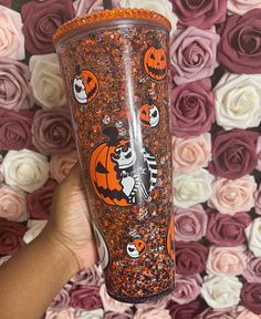 someone holding up a halloween themed tumbler with sprinkles and pumpkins on it