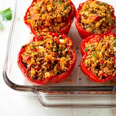 four stuffed red peppers in a baking dish with seasoning on the top and green sprigs