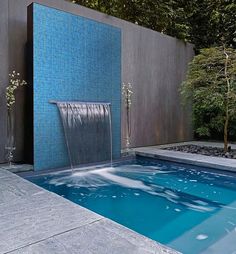 a small pool with a waterfall in the middle and blue tiles on the wall behind it