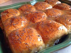 a green casserole dish filled with rolls covered in cheese and black sesame seeds