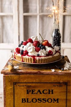 a pie with berries and whipped cream on top sitting on a wooden box next to a bottle of wine