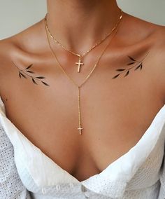 a woman's chest with cross and arrow tattoos on her upper arm, behind her is a white blouse