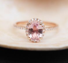 an oval shaped pink sapphire and diamond ring sits on a seashell with its shell in the background