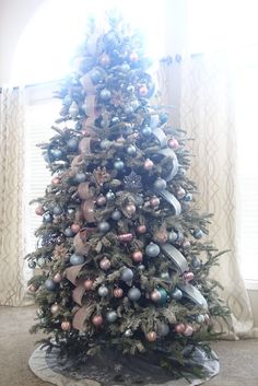 a decorated christmas tree sitting in front of a window with ribbon and ornaments on it