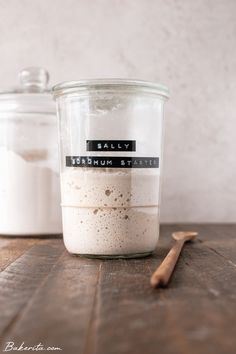 a glass jar filled with food sitting on top of a wooden table next to a spoon