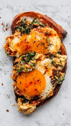 an open face sandwich with eggs and spinach sprinkled on top, sitting on a marble surface