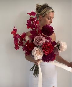 a woman in a white dress holding a bouquet of red, pink and purple flowers