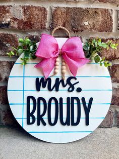 a wooden sign that says mrs broddy with a pink bow hanging on the side of a brick wall